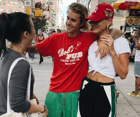 A man in a red shirt and a woman in a red cap pose smiling with another woman on a busy city street.