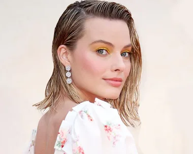 Margot Robbie as Sharon Tate with wet hair, floral dress, and yellow eye makeup.