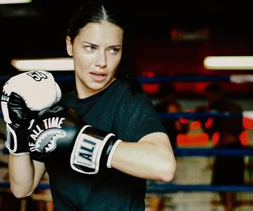 A woman in boxing gloves practicing in a gym.