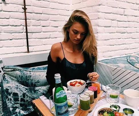 Woman eating healthy meal at outdoor cafe with drinks and vegetables.