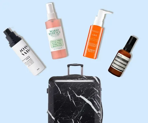 A collection of skincare products including Mario Badescu Facial Spray, near a black marble suitcase on a light blue background.