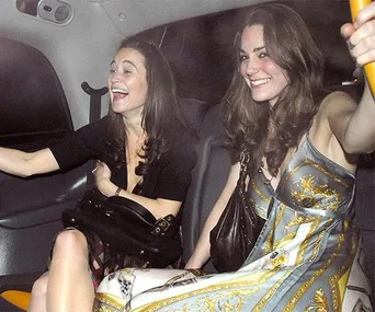 Two women smiling and laughing inside a car, one wearing a patterned dress and the other holding a handbag.