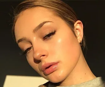 Close-up of a person with glowing skin, wearing makeup, and looking directly at the camera in natural light.