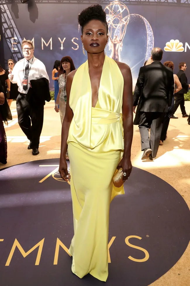 Woman in a yellow gown holding a clutch at the Emmy Awards red carpet.