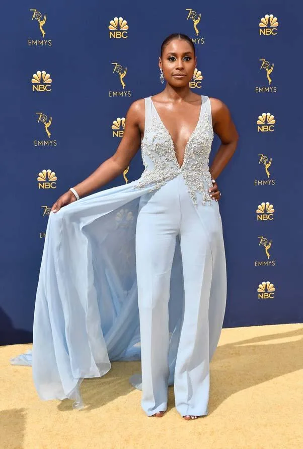 Woman in a light blue outfit with deep neckline and flowing cape on red carpet at 70th Emmy Awards.
