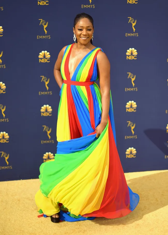 Woman in a colorful striped gown at the Emmys with a dark blue background featuring the NBC logo and Emmy statuettes.