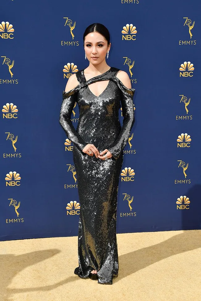 A woman in a shimmering black gown poses on the red carpet at the 70th Emmy Awards with NBC logos in the background.