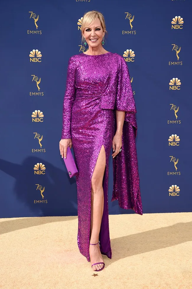 Person in a shimmering purple dress poses on the Emmy Awards red carpet with a matching clutch.