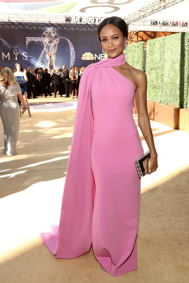 Person in a pink gown at an outdoor event, standing on a beige carpet with a crowd in the background.