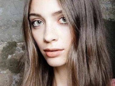 Close-up of a woman with long, straight brown hair and green eyes, showcasing her clear skin and natural makeup.