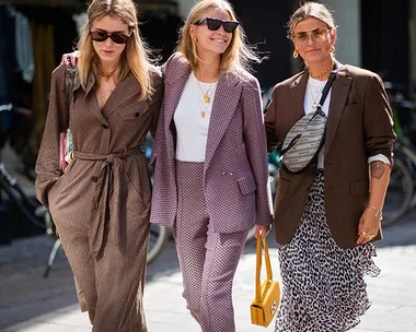 Three women in stylish outfits, including blazers and sunglasses, walking together during fashion week.