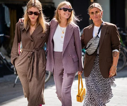 Three women in stylish outfits, including blazers and sunglasses, walking together during fashion week.