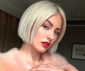 A woman with a platinum blonde bob, red lipstick, wearing a pink fur coat.