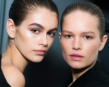 Two models with slicked-back hair showing smooth, glowing skin, one with dark features and the other with fair features.