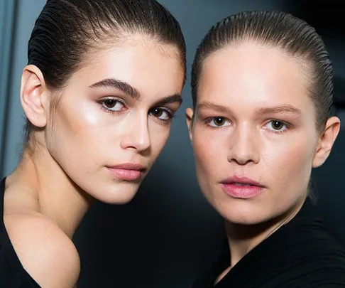 Two models with slicked-back hair showing smooth, glowing skin, one with dark features and the other with fair features.