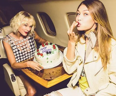 Two women on a private jet with a birthday cake; one is eating and the other is holding the cake.