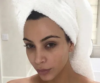 A person with a towel wrapped around their head posing without makeup in a bathroom setting.