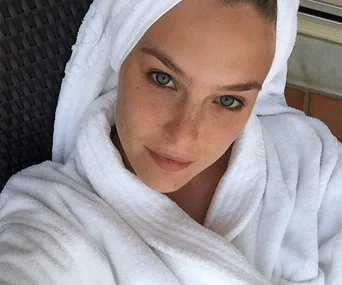 Person in a white robe and towel turban, looking relaxed with clear skin, possibly related to skincare or cleansing products.