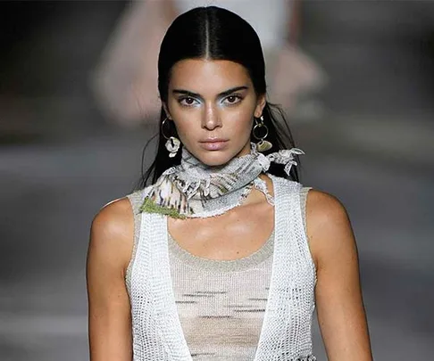 A model on the runway wearing a knit tank top and a scarf around her neck.