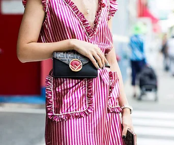 Woman in red and white striped dress with black clutch, crossing street.