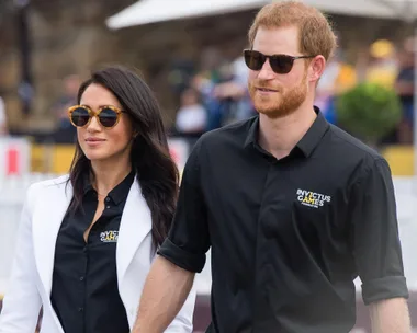 Prince Harry and Meghan Markle at Invictus Games, both wearing sunglasses and Invictus Games shirts.