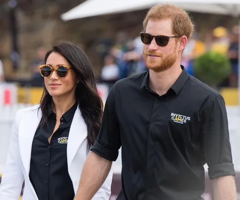 Prince Harry and Meghan Markle at Invictus Games, both wearing sunglasses and Invictus Games shirts.