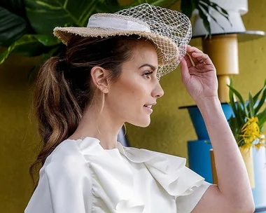 Woman in white dress and hat with veil, smiling and looking to the right, with vibrant background decor.