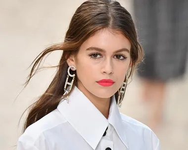 Young woman with smooth, straight hair wearing large earrings and a white collared shirt.