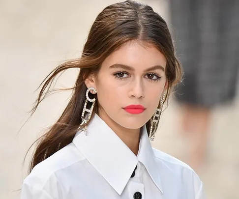 Young woman with smooth, straight hair wearing large earrings and a white collared shirt.