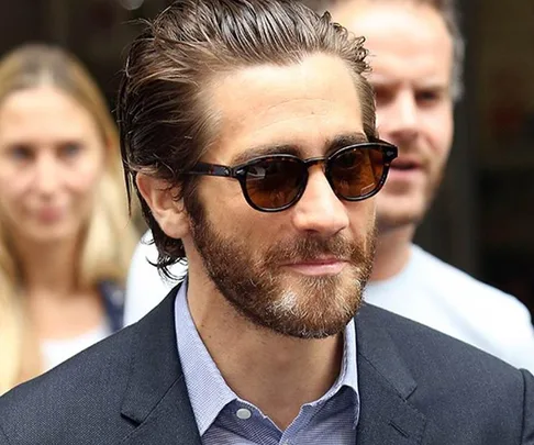 Man with sunglasses, thick beard, slicked-back hair in a suit.