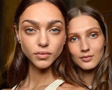 Two women with similar bronzed makeup and long hair, posing closely together.