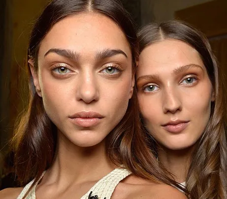 Two women with similar bronzed makeup and long hair, posing closely together.