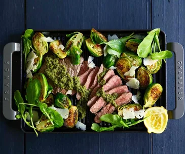 Grilled steak slices with Brussels sprouts, spinach, and pesto sauce on a black Chasseur grill pan.