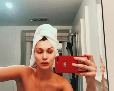 Woman with a towel on her head takes a mirror selfie in the bathroom with a red phone.