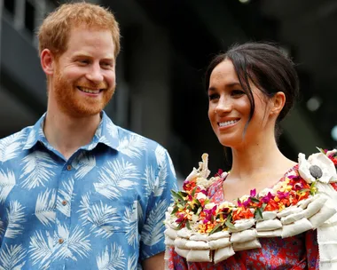 Prince Harry and Meghan Markle smiling and wearing colorful, tropical-themed outfits.