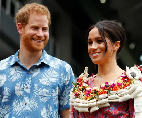 Prince Harry and Meghan Markle smiling and wearing colorful, tropical-themed outfits.