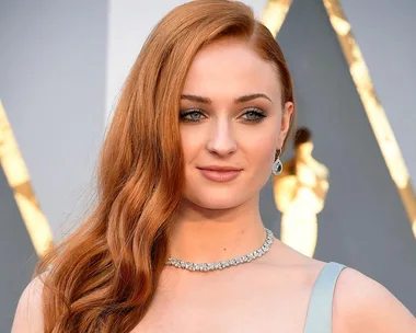 Woman with long red hair, wearing a necklace and earrings, at a formal event.