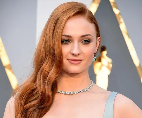 Woman with long red hair, wearing a necklace and earrings, at a formal event.