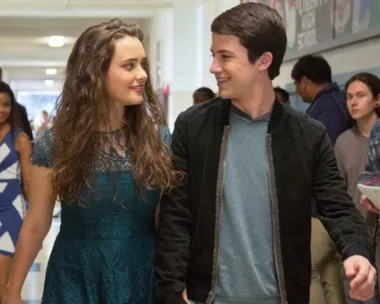 Two teenagers walking in a school hallway, smiling at each other, from "13 Reasons Why".