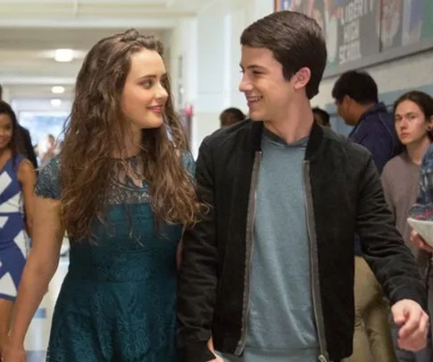 Two teenagers walking in a school hallway, smiling at each other, from "13 Reasons Why".