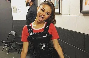 Young woman in a red top and black overalls playfully sticking out her tongue backstage.