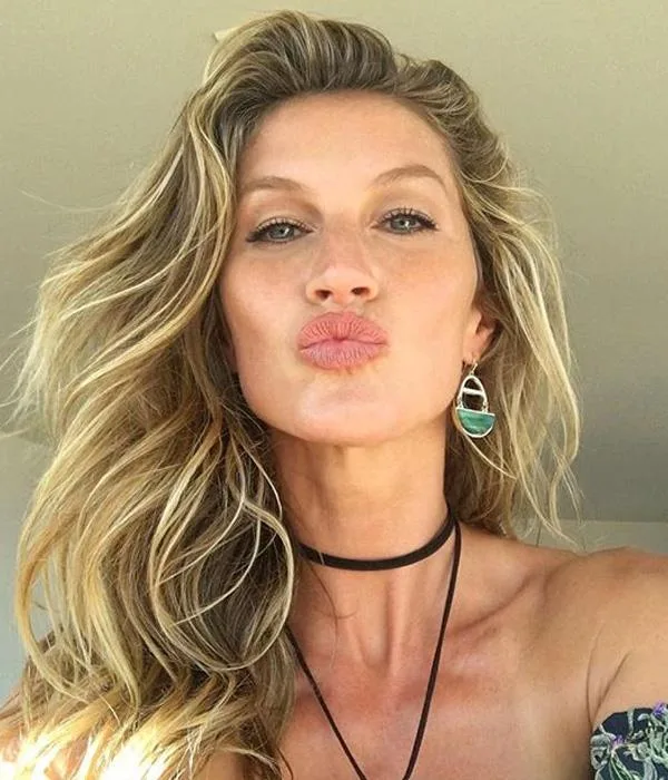 Blonde woman blowing a kiss towards the camera, wearing earrings and a choker.