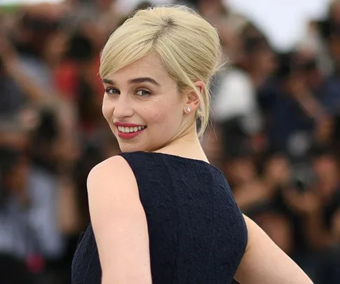 A woman with blonde hair smiling and looking over her shoulder at a formal event, with a crowd in the background.