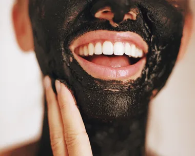 A person smiling while applying a black charcoal face mask.