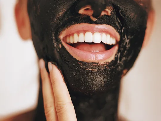 A person smiling while applying a black charcoal face mask.