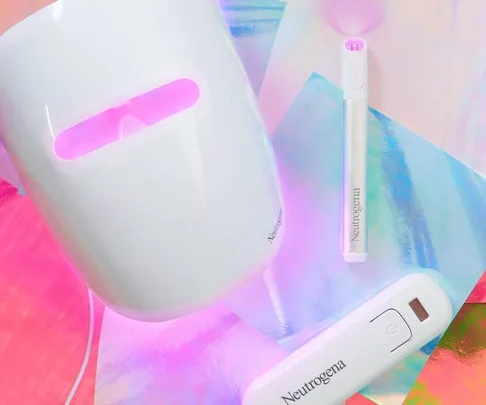 Neutrogena Light Therapy Acne Mask, activated and glowing, with treatment wand and activator against a vibrant holographic background.