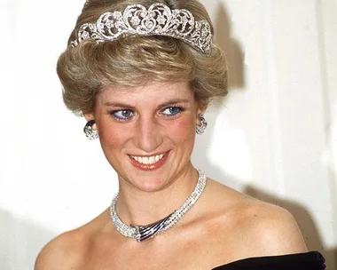 A woman wearing a sparkling tiara and necklace, smiling at an event.