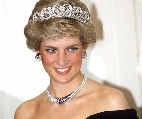 A woman wearing a sparkling tiara and necklace, smiling at an event.