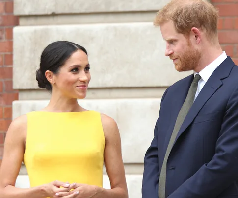 A woman in a yellow dress and a man in a suit standing together, exchanging smiles.