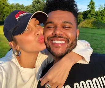 Two people posing for a cheerful selfie outdoors, one kissing the other's cheek.